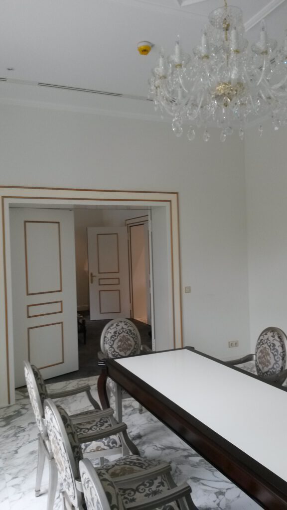 Eleganter Altbau-Innenraum mit Kronleuchter, historischen Türen und Marmorboden nach den Vorgaben für eine denkmalschutzgerechte Renovierung in Berlin saniert.